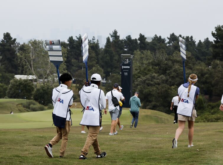 LOS ANGELES, CA - JUNE 14: Sign bearers walk the 15th fairway with a cloudy downtown skyline during the practice rounds at The Los Angeles Country Club on Wednesday, June 14, 2023 in Los Angeles, CA. (Gina Ferazzi / Los Angeles Times)