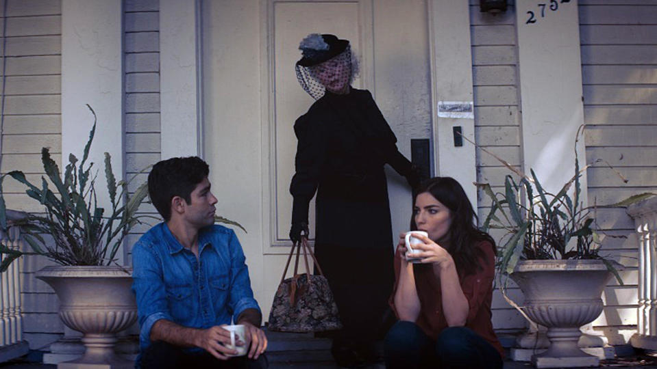 A couple drinks coffee on a porch while a grieving woman arrives on the doorstep