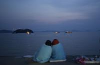 Relatives of passengers aboard the sunken ferry Sewol sit near the sea at a port in Jindo, south of Seoul, South Korea, Sunday, April 20, 2014. After more than three days of frustration and failure, divers on Sunday finally found a way into the submerged ferry off South Korea's southern shore, discovering more than a dozen bodies inside the ship and pushing the confirmed death toll to over four dozens, officials said. (AP Photo/Lee Jin-man)