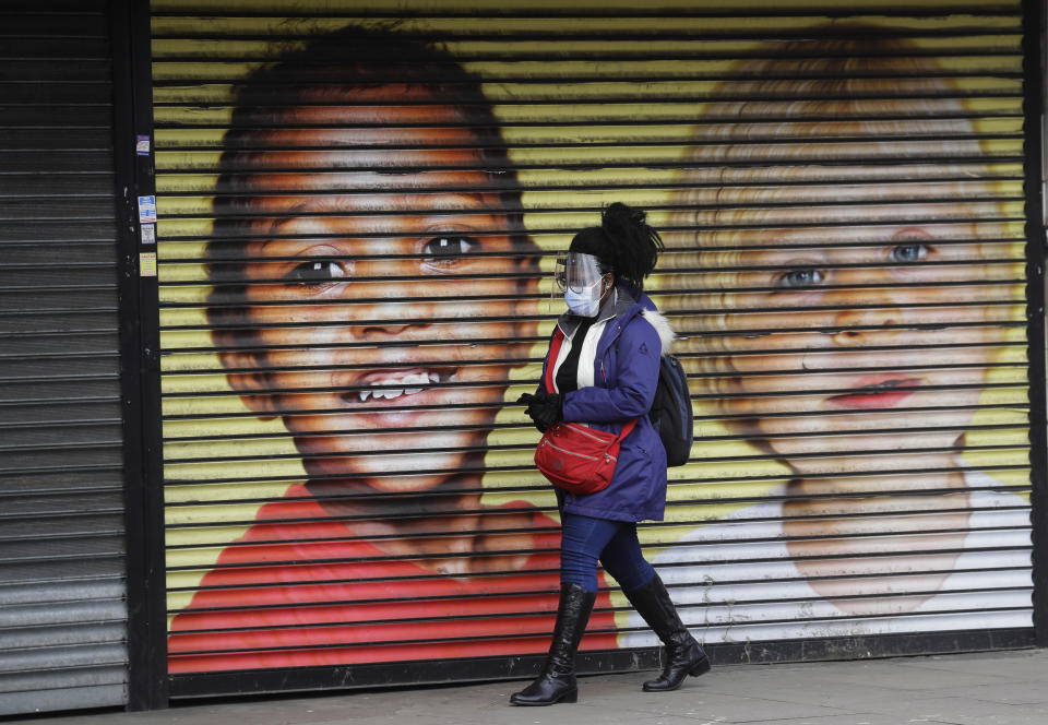 A woman wears protective face coverings as she passes the shutters of a closed shop in West Ealing in London, Thursday, Feb. 25, 2021. It has been announced that further testing of residents in the London Borough of Ealing will be carried out after additional cases of the coronavirus variant first identified in South Africa were detected. (AP Photo/Kirsty Wigglesworth)