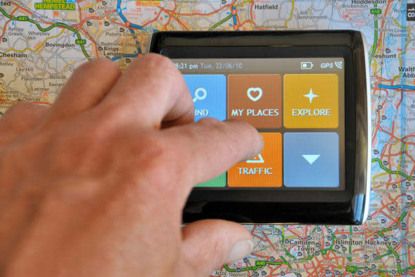 a sat nav sits on a road map with a hand using the touch screen to find information regarding road traffic.