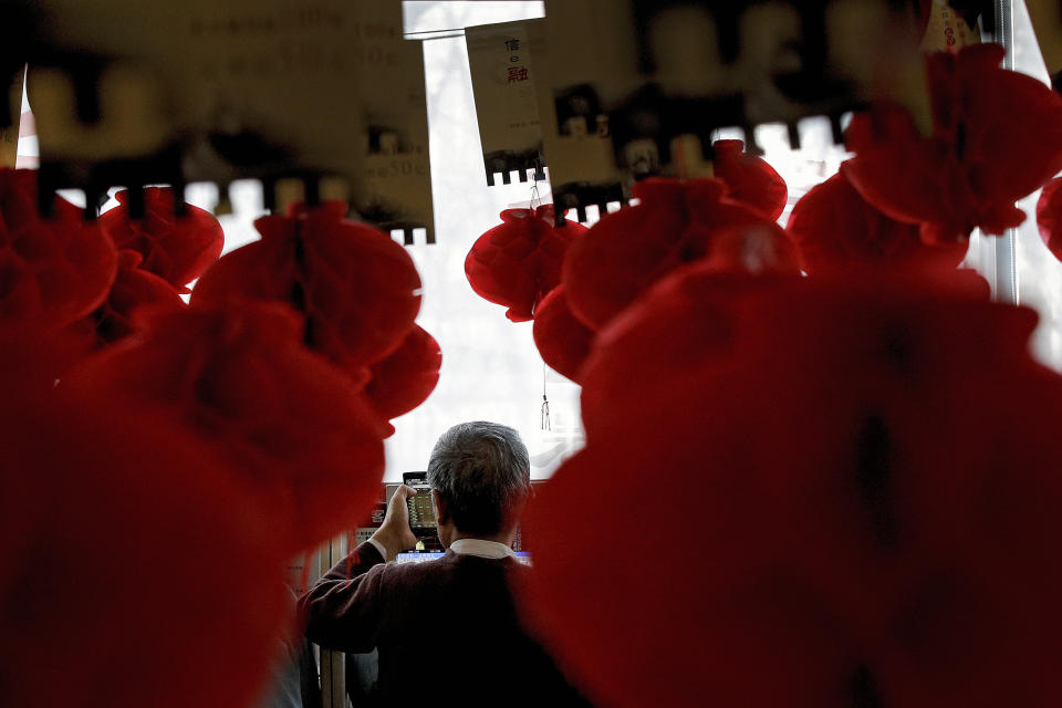 A man holds a smartphone showing stock prices as he monitors stock prices at a brokerage house decorated with red lanterns in Beijing, Friday, Feb. 1, 2019. Asian markets were mixed on Friday as trade talks ended in Washington with no deal but the promise of a second meeting between U.S. President Donald Trump and Chinese leader Xi Jinping. Gains were limited by a private survey showing that Chinese manufacturing slowed to the lowest level in almost three years. (AP Photo/Andy Wong)