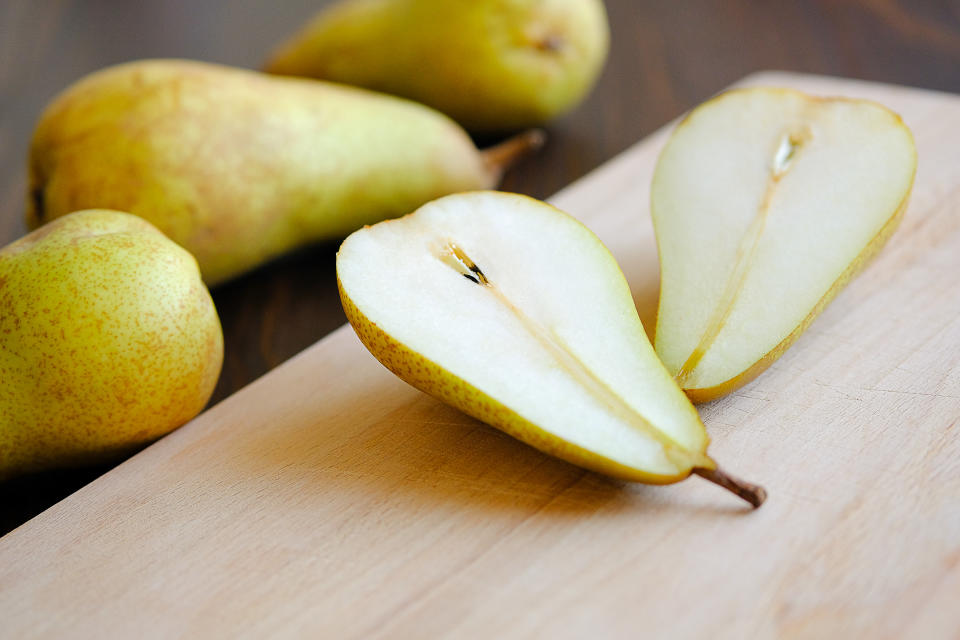 Sliced halves or slices of fresh sweet ripe yellow and green pears, next whole pears and cutting kitchen Board on a brown wooden table background, close-up. Vegetarian and vegan food.