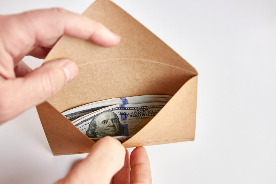 Hands holding an open envelope filled with hundred-dollar bills