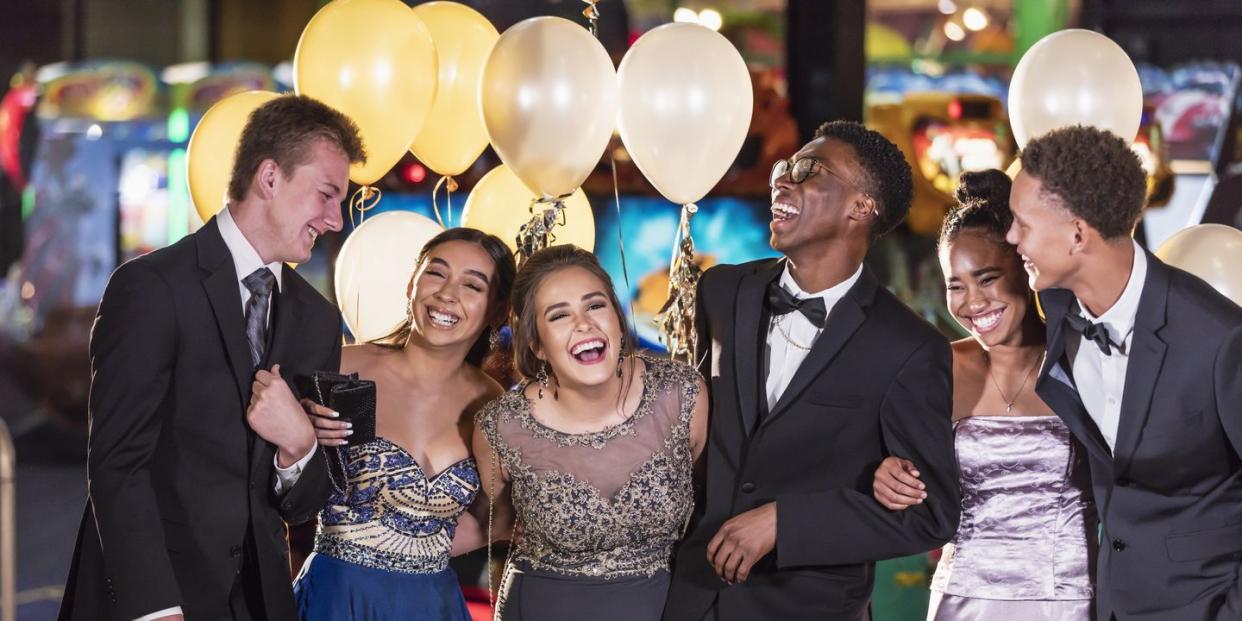 a multi ethnic group of six teenagers, three multi ethnic couples, having fun at their high school prom the two girls are wearing prom dresses and their dates are wearing a suit and tuxedo