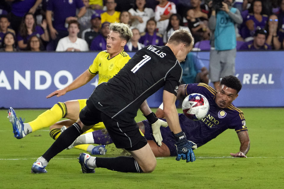 Nashville SC goalkeeper Joe Willis (1) blocks a shot-attempt by Orlando City midfielder Junior Urso, right, as Nashville SC defender Lukas MacNaughton, left, tries to help during the second half of an MLS playoff soccer match, Monday, Oct. 30, 2023, in Orlando, Fla. (AP Photo/John Raoux)