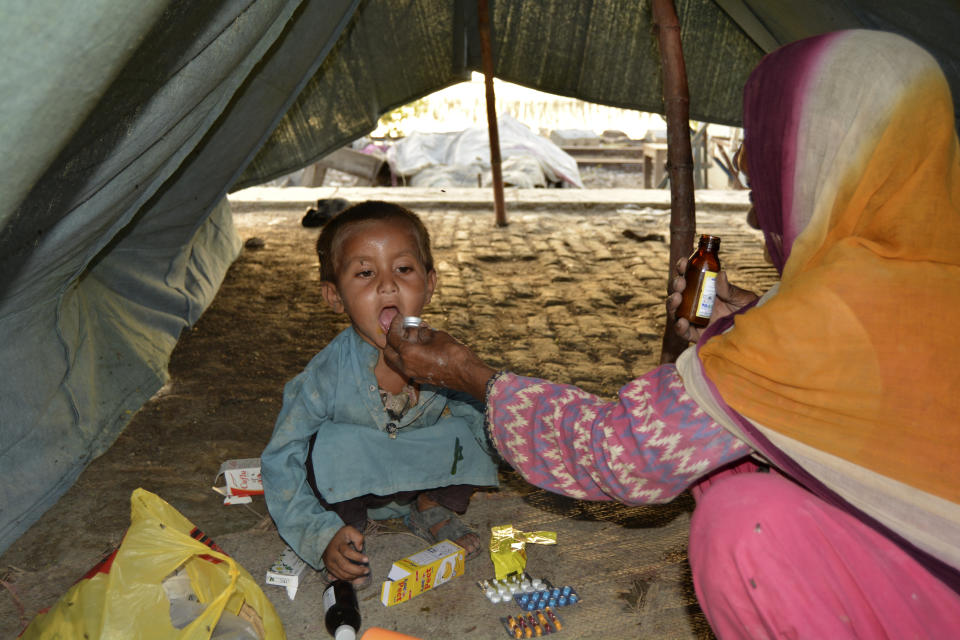 A displaced woman gives a medicine to her son as she fled her flood-hit home in Rajanpur a district of Punjab province of Pakistan, Friday, Sep. 2, 2022. Planes carrying fresh supplies are surging across a humanitarian air bridge to flood-ravaged Pakistan as the death toll surged past 1,200, officials said Friday, with families and children at special risk of disease and homelessness. (AP Photo/Shazia Bhatti)