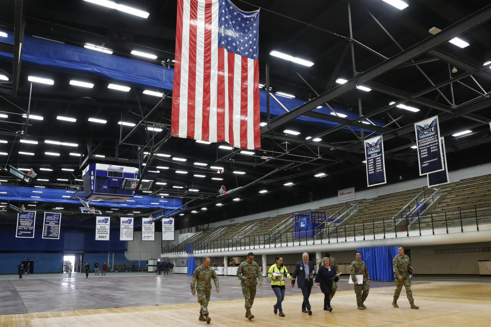 National Guard personnel join Yale New Haven Health officials walk across the court at Southern Connecticut State University's Moore Field House as they prepare to survey supplies delivered by FEMA for a "surge" hospital to help out during the current coronavirus crisis, Tuesday, March 31, 2020, in New Haven, Conn. The 250-bed field hospital will facilitate overflow in the event that regional hospitals treating COVID-19 patients reach their capacity. (AP Photo/Kathy Willens)