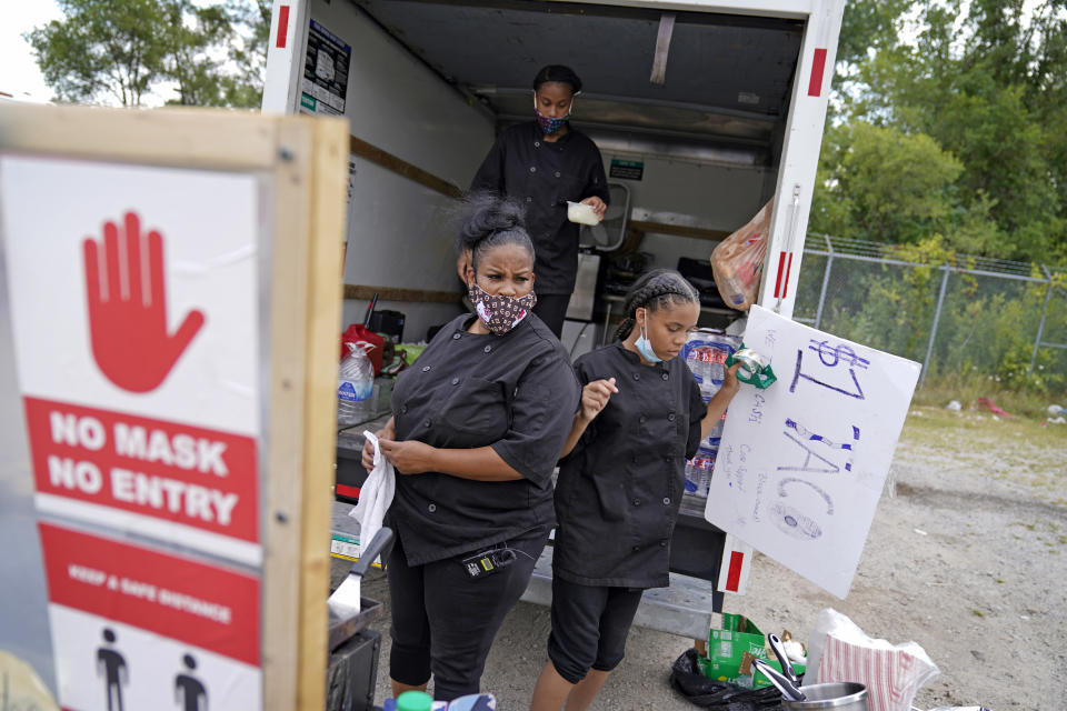 Tequila Butler, left, sets up her taco stand out of the back of a U-Haul truck with her daughters, Alliyah, 15, rear, and Chardonnay, 14, in the Auburn Gresham neighborhood in Chicago, Thursday, Aug. 27, 2020. Butler suspects she was infected with the virus this spring after she was transferred from her job in a hospital kitchen to one cleaning COVID-19 patients' rooms. After she was furloughed, she decided not to go back. So the culinary school graduate converted a rented U-Haul into a truck that sells $1 tacos, the low price to accommodate customers with little money.(AP Photo/David Goldman)