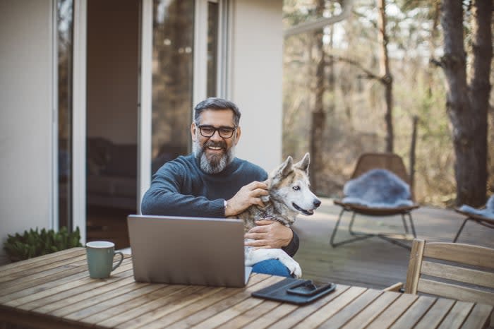 A person at a laptop holding a dog.