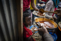 Elena, 7, center, lines up with other displaced Tigrayans to receive food donated by local residents at a reception center for the internally displaced in Mekele, in the Tigray region of northern Ethiopia, on Sunday, May 9, 2021. The 15 kilograms of wheat, half a kilogram of peas and some cooking oil per person, to last a month — was earmarked only for the most vulnerable. That included pregnant mothers and elderly people. (AP Photo/Ben Curtis)