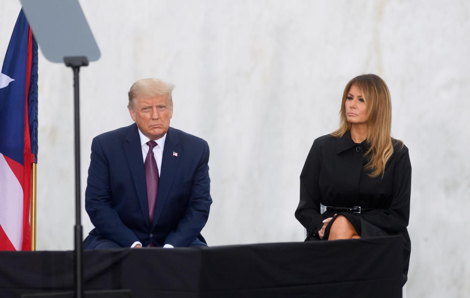 Donald Trump in a dark suit and Melania Trump in a black dress seated next to each other at an event