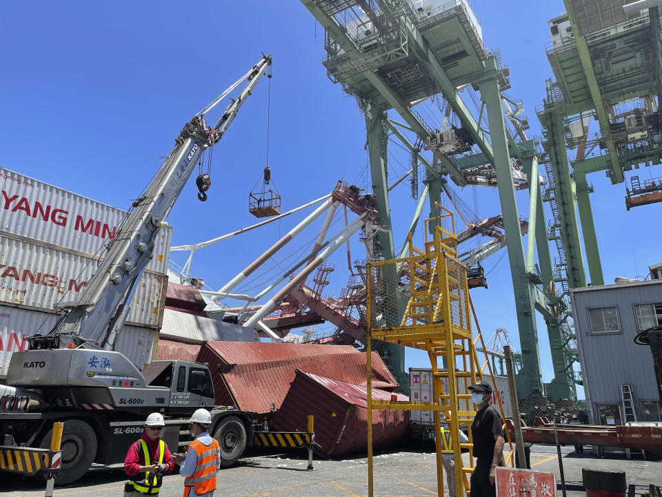 Port workers view the scene of a massive container gantry crane that toppled over Thursday, June 3, 2021, in the port of Khaohsiung, southern Taiwan. The crane fell over after a cargo ship knocked into it Thursday morning, sending it crashing to the ground in the port. (Taiwan International Ports Corporation Ltd. via AP)