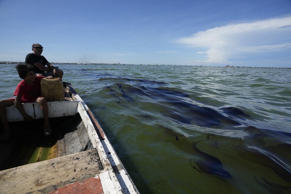 El pescador Óscar Luzardo navega en su bote y pasa al lado de una mancha de crudo en el Lago de Maracaibo, cerca del municipio de San Francisco, Venezuela, el jueves 10 de agosto de 2023. Antes famoso por sus aguas cristalinas, el lago se convirtió en un entorno contaminado por derrames de crudo de deteriorados oleoductos y plataformas. (AP Foto/Ariana Cubillos)