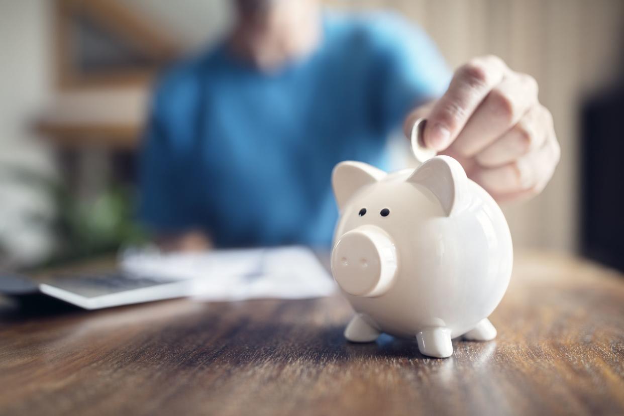 Man putting a coin into a pink piggy bank concept for savings and finance