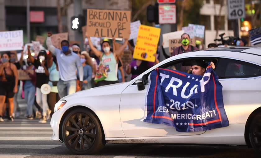 LOS ANGELES, CALIFORNIA SEPTEMBER 26, 2020-A driver holds a Trump flag outside his car as supporters for Breonna Taylor march at the intersection of Ventura and Sepulveda Blvd.'s in Serman Oaks Saturaday. The supporters marched around the intersection 26 times in honor of her age before being killed by police. (Los Angeles Times/Wally Skalij)