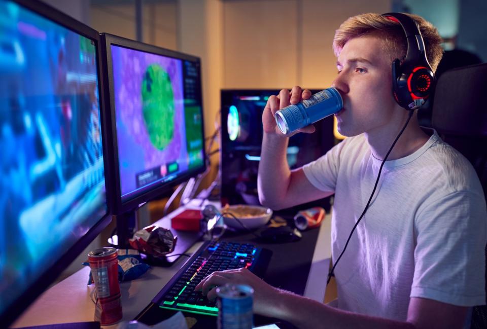 Person playing video games on a computer with two large monitors while drinking an energy drink.