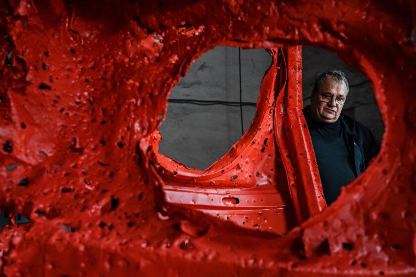 Ukrainian sculptor Mikhail Reva looks through a red sculpture fashioned from part of a destroyed Russian military vehicle.