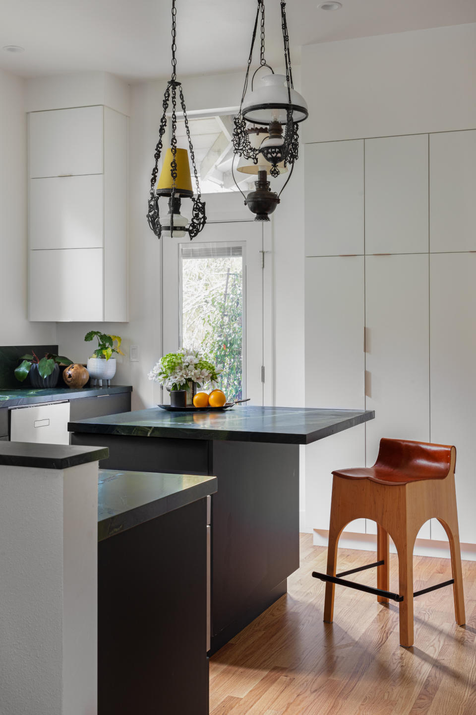 Black kitchen cabinets and square island with dark green marble countertop