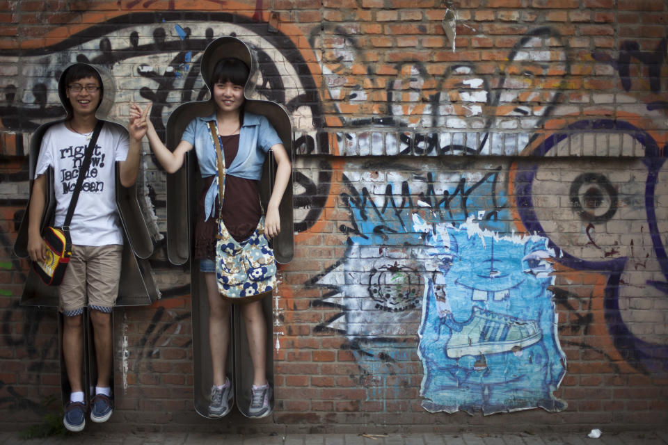 In this Thursday, July 12, 2012 photo, a couple hold their hands in female and male body shaped metal frames installed on a wall while posing for photos at the 798 Art District in Beijing, China. The city's art district, often compared to New York City's Greenwich Village, is a thriving community of about 400 galleries, shops and restaurants on the eastern edge of Beijing housed in a complex of former electronics factories built with the help of East Germany in the 1950s. (AP Photo/Alexander F. Yuan)