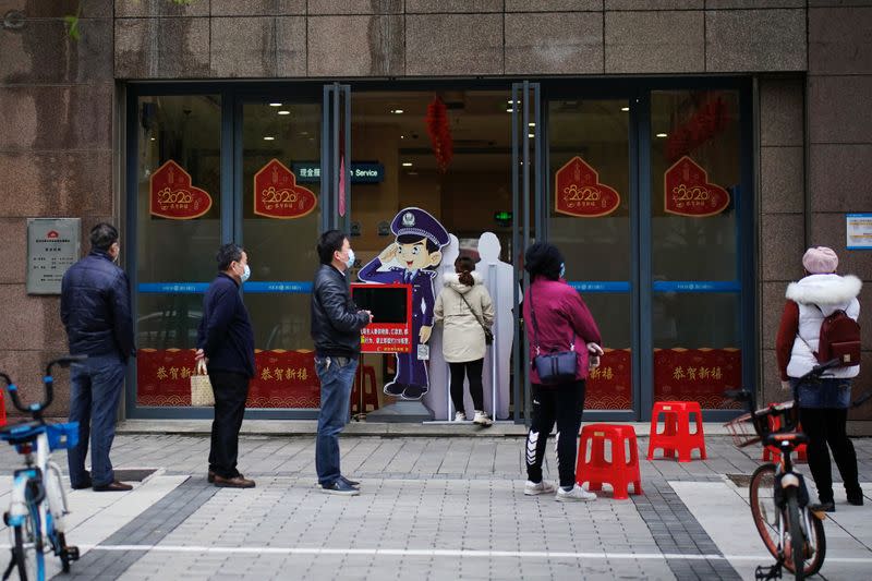 People wearing face masks practise social distancing as they wait outside a Hankou Bank branch in Wuhan