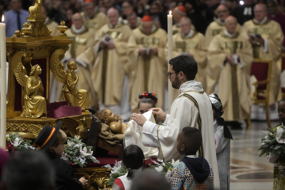 A priest unveils a statue of Baby Jesus as Pope Francis presides over Christmas Eve Mass, at St. Peter's Basilica at the Vatican, Saturday Dec. 24, 2022. (AP Photo/Gregorio Borgia)