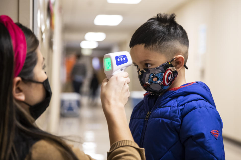 FILE - In this Jan. 11, 2021, file photo, a preschool student gets his temperature checked as he walks into Dawes Elementary School in Chicago. Pressure is building on school systems around the U.S. to reopen classrooms to students who have been learning online for nearly a year, pitting politicians against teachers who have yet to be vaccinated against COVID-19. (Ashlee Rezin Garcia/Chicago Sun-Times via AP, Pool, File)