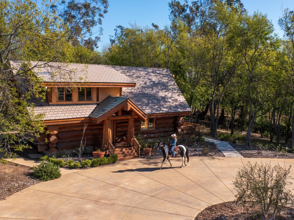 A home with someone on a horse riding past it.