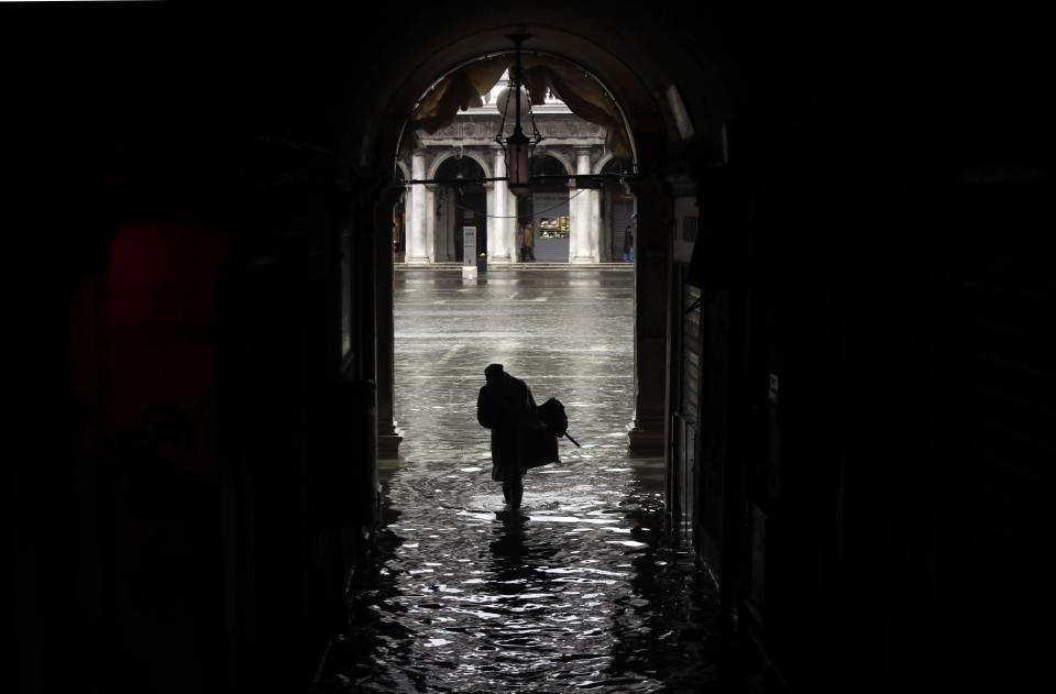 A woman is silhouetted as she walks towards a flooded St. Mark's Square, on the occasion of a high tide, in Venice, Italy, Tuesday, Nov. 12, 2019. The high tide reached a peak of 127cm (4.1ft) at 10:35am while an even higher level of 140cm(4.6ft) was predicted for later Tuesday evening. (AP Photo/Luca Bruno)