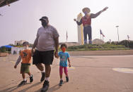 Wearing face masks to prevent the spread of COVD-19, Trey Lipscomb, center, holds the hands of his son, Trey, 6, and daughter Tia, 4, as they walk in front of Big Tex after getting their photo made during a visit to Fair Park in Dallas, Saturday, Sept. 19, 2020. Although the State Fair of Texas was canceled this year, fair organizers are holding drive-thru visits starting this weekend. (AP Photo/LM Otero)