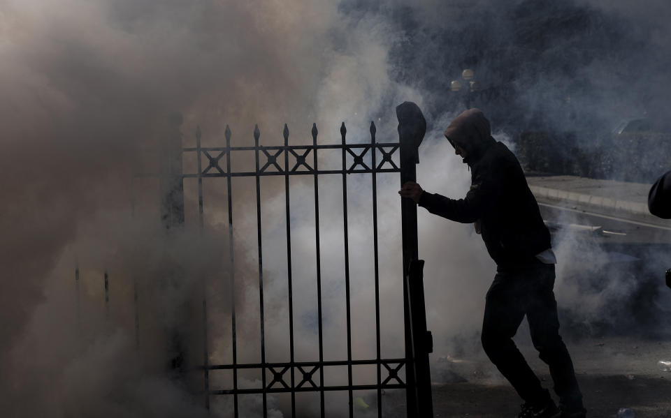 A protester pushes a gate amid smoke from teargas during an anti-government rally in Tirana, Albania, Saturday, March 16, 2019. Albanian opposition supporters clashed with police while trying to storm the parliament building Saturday in a protest against the government which they accuse of being corrupt and linked to organized crime. (AP Photo/Hektor Pustina)