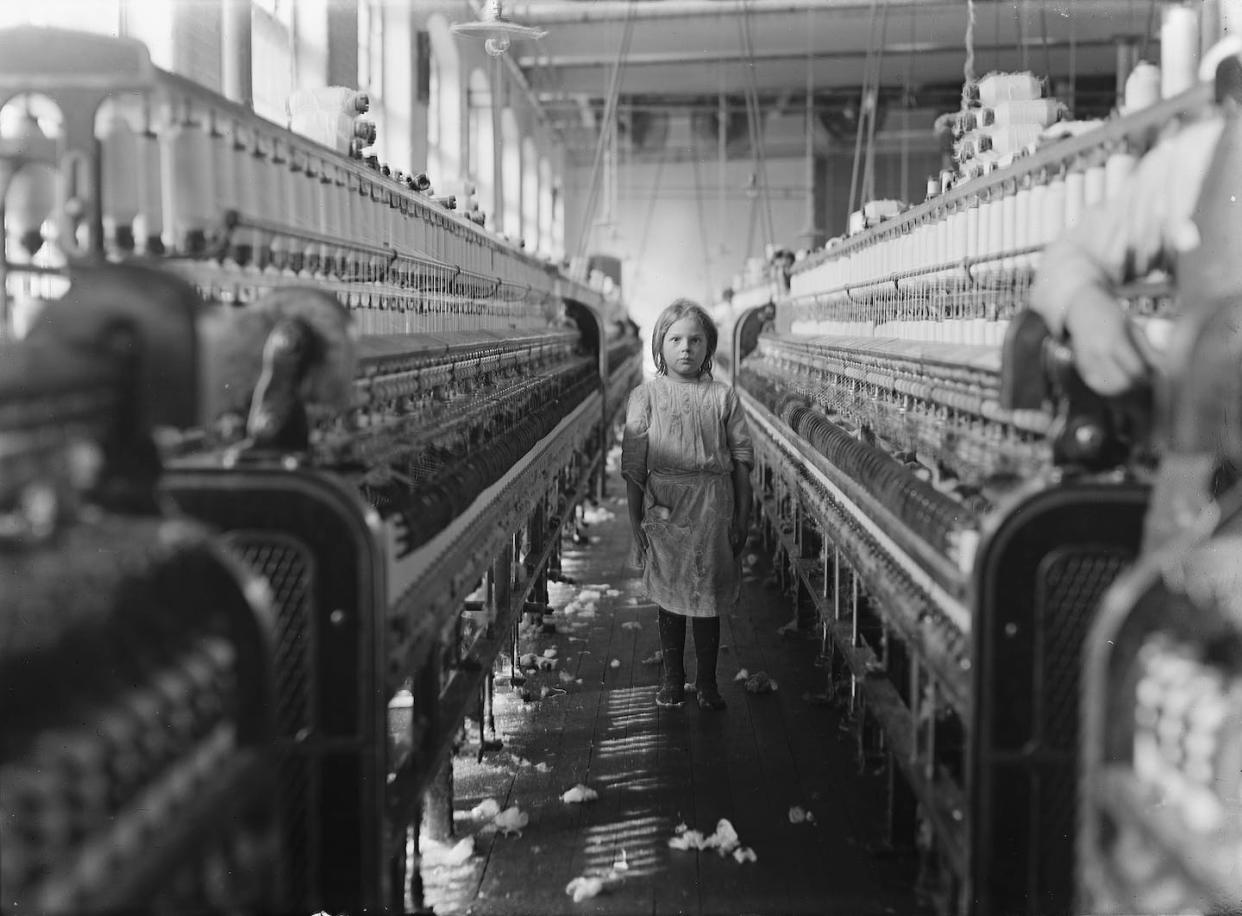 Photograph by Lewis W. Hine of a small spinner at Mollohan Mills, Newberry, S.C.: "She was tending her 'sides' like a veteran, but after I took the photo, the overseer came up and said in an apologetic tone that was pathetic, 'She just happened in.' Then a moment later he repeated the information. The mills appear to be full of youngsters that 'just happened in,' or 'are helping sister.' <a href="https://commons.wikimedia.org/wiki/File:Child_laborer.jpg" rel="nofollow noopener" target="_blank" data-ylk="slk:National Child Labor Committee/Library of Congress;elm:context_link;itc:0;sec:content-canvas" class="link ">National Child Labor Committee/Library of Congress</a>