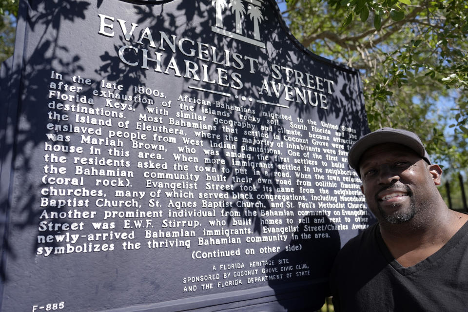 Resident Charles Gibson stands next to a plaque commemorating the Bahamian roots of the Miami neighborhood of west Coconut Grove, Friday, April 5, 2024. The majority-Black neighborhood — known by names such as West Grove, Black Grove, or even Little Bahamas, in a nod to its Bahamian roots — has nurtured the early careers of numerous notable sports figures, from Olympic Gold medalists to NFL Hall of Famers like Frank Gore and Amari Cooper, as well as housed successful Black business owners and stalwarts who played a vital role in city's history and culture. (AP Photo/Lynne Sladky)