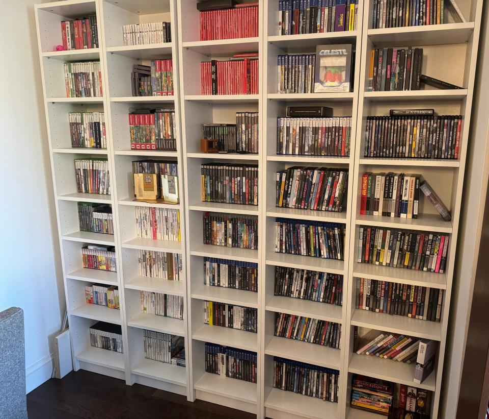 five tall white bookshelves, filled with video games, and dvds