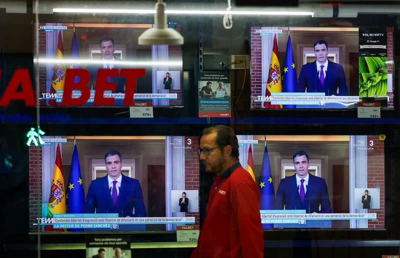 A person walks next to TVs broadcasting the statement by Spain's Prime Minister Sanchez, in El Masnou, north of Barcelona