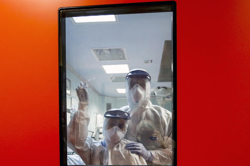 Medical staff wave from inside the ICU unit of the Covid 3 hospital in Casalpalocco, near Rome, Saturday, April 11, 2020. Italy has topped 19,000 deaths and 150,000 cases of coronavirus. The milestones were hit Saturday, even as the country continued to see a slight decrease in numbers of people hospitalize and in intensive care. The new coronavirus causes mild or moderate symptoms for most people, but for some, especially older adults and people with existing health problems, it can cause more severe illness or death. (Cecilia Fabiano/LaPresse via AP)