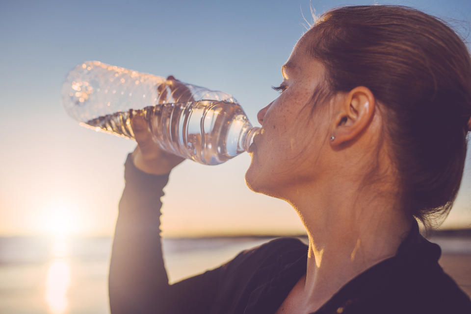 Woman drinking water seaside after running at the beach.