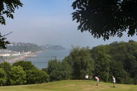 People play on one of the greens of the pitch and put golf course in Shaldon, Devon, England, Thursday July 22, 2021. In the background is Teignmouth and the pier. (AP Photo/Tony Hicks)