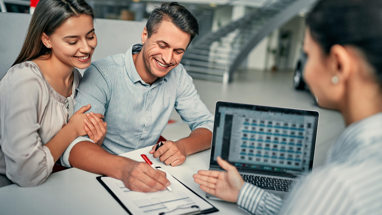 Beautiful young couple signs documents at dealership showroom.