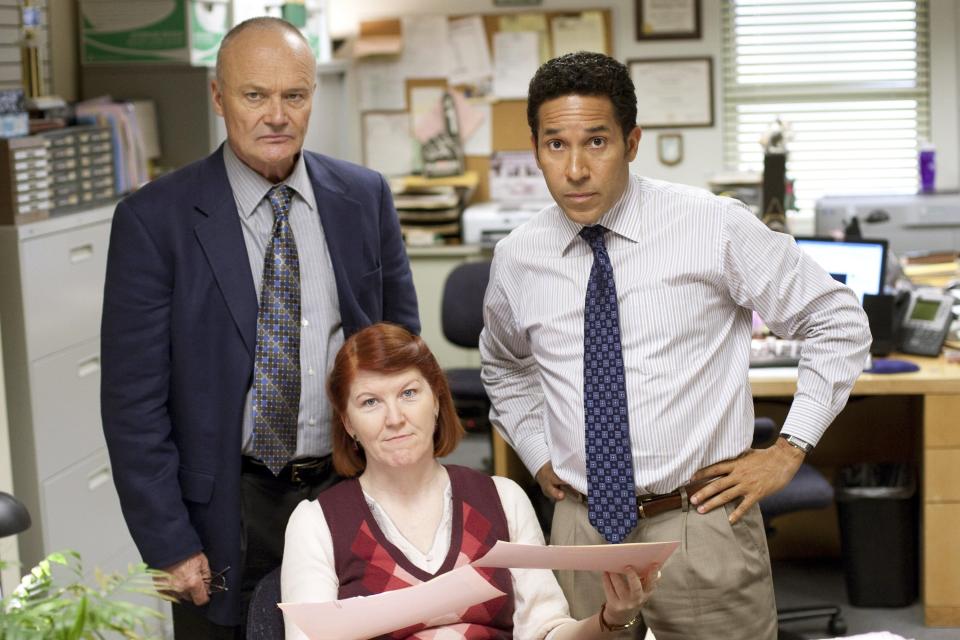 Creed Bratton, Kate Flannery, and Oscar Nunez from "The Office" standing in an office setting, looking serious