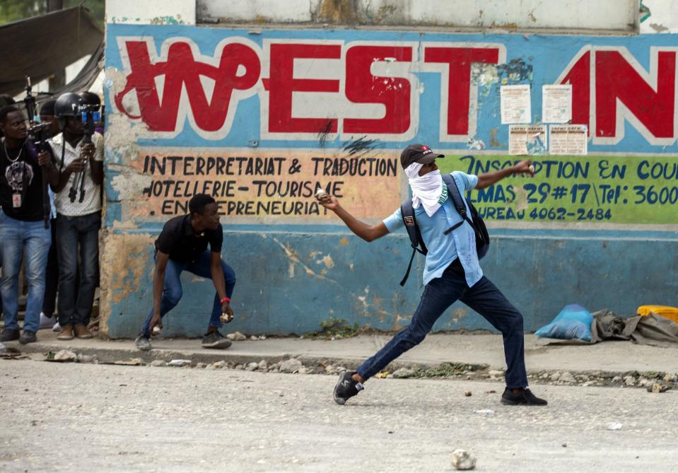 A masked protester throws rocks at police attempting to disperse protesters demanding answers after the kidnapping and murder of high school senior Evelyne Sincère, in Port-au-Prince, Haiti, Thursday, Nov. 5, 2020. The young woman was found in a trash heap Sunday after relatives said they were unable to pay the large ransom demanded by her captors. Human rights groups contend the incident highlights the nation’s worsening security crisis. (AP Photo/Dieu Nalio Chery)