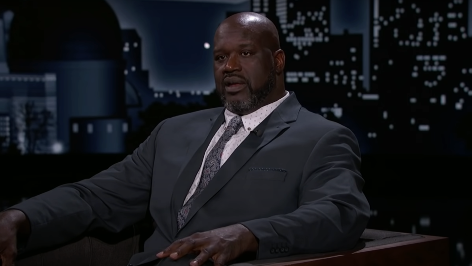 Shaquille O'Neal in a talk show setting, wearing a suit and patterned tie