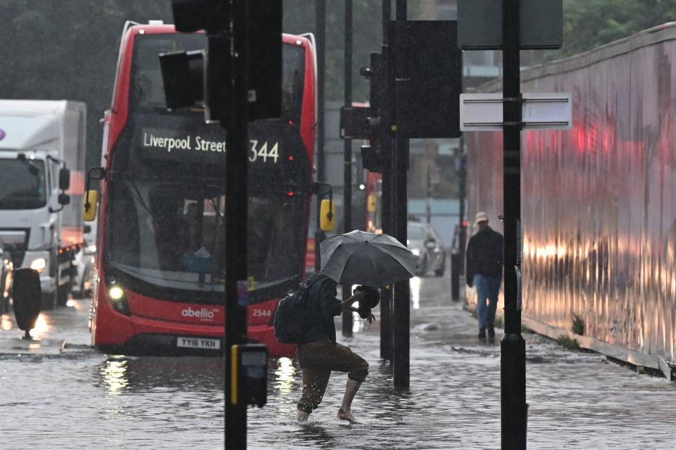 <p>A pedestrian crosses through deep water on a flooded road in The Nine Elms district of London on July 25, 2021 during heavy rain. - Buses and cars were left stranded when roads across London flooded on Sunday, as repeated thunderstorms battered the British capital. (Photo by JUSTIN TALLIS / AFP) (Photo by JUSTIN TALLIS/AFP via Getty Images)</p>
