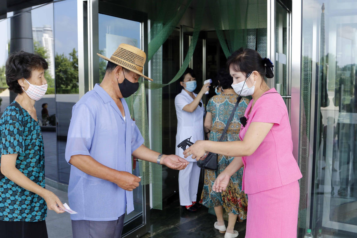 Two employees of the Ryugyong Health Complex disinfect the hands and check the fever of people coming to the complex to help curb the spread of the coronavirus, in Pyongyang, North Korea, Friday, July 31, 2020. (AP Photo/Jon Chol Jin)