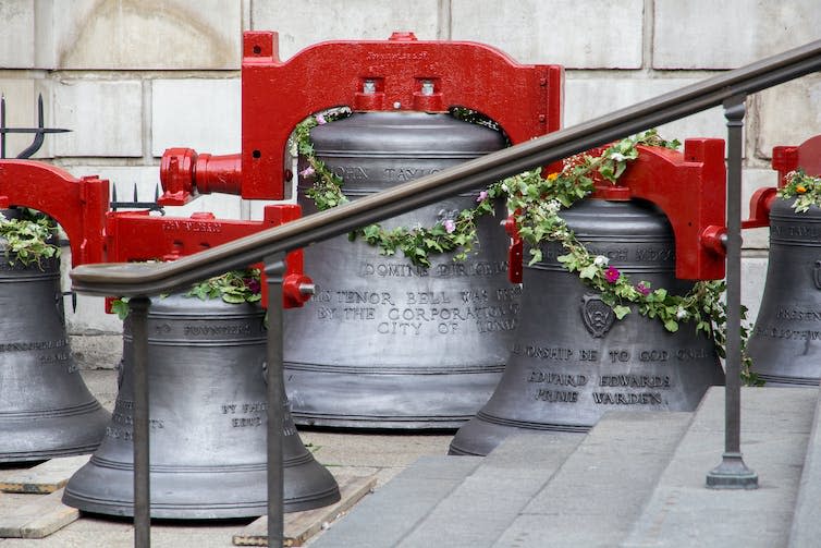 Large metal bells with red fixtures on the pavement.