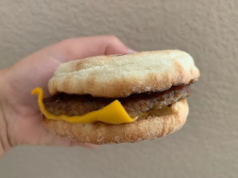 hand holding a sausage McMuffin with cheese in front of beige wall