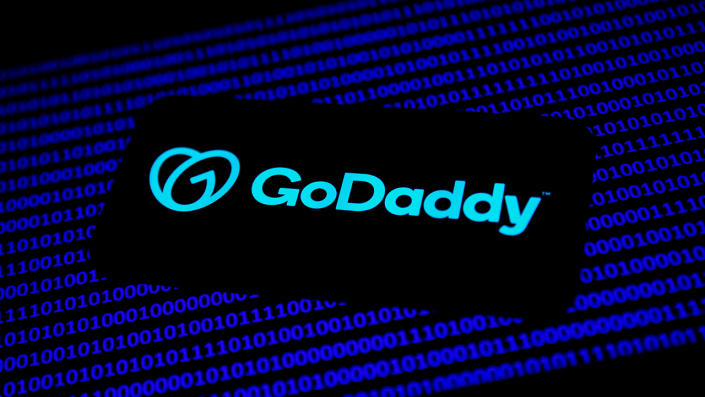 GoDaddy logo displayed on a phone screen and binary code displayed on a laptop screen are seen in this illustration photo.