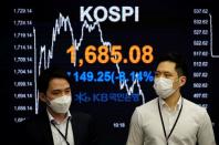 Currency dealers walk past an electronic board showing the Korea Composite Stock Price Index (KOSPI) at a dealing room of a bank in Seoul