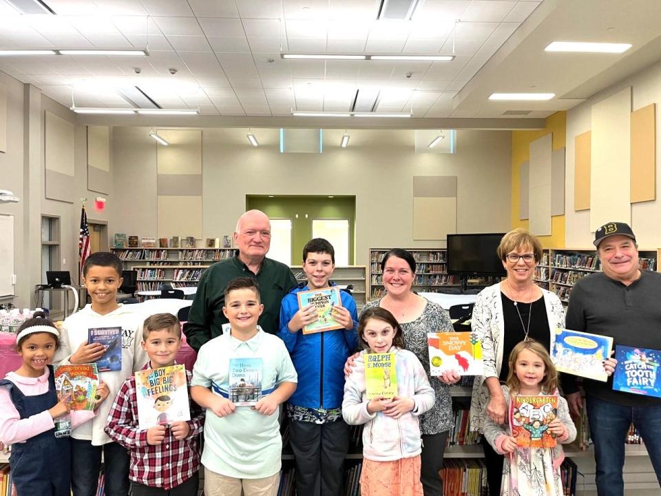 From left, Mulcahey Elementary School students 
Payce Pawlowski, Brock Pawlowski, Ethan Silveira and 
Julian Silveira; Maureen Drake's husband Frank Drake; Frank and Maureen's grandson Drake Charbonneau; their granddaughter Hannah Charbonneau; their daughter Janine Charbonneau; Maureen Drake's childhood friend Anne Marie Rodrigues; Rodrigues' granddaughter, Mulcahey student Ava Letourneau; and Maureen Drake's brother Randy Silveira are on hand at Mulcahey Elementary School in Taunton on Wednesday, Nov. 16, 2022, for a book giveaway in honor of the late Maureen Drake, a retired Mulcahey teacher.