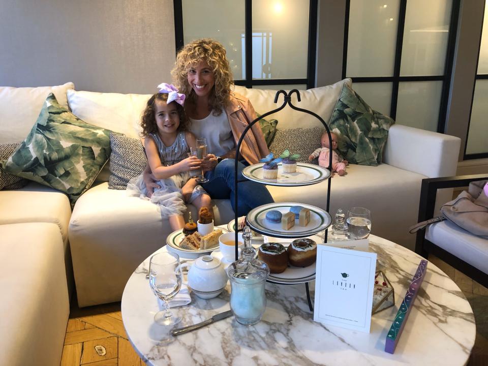 A woman and her daughter sitting on a couch with a tea tray of pastries.